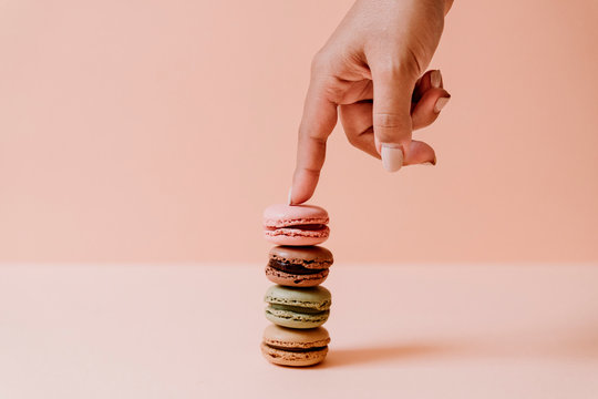 Female hand touching stack of macaroons on pink background