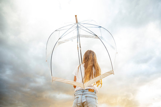 Blond girl holding transparent umbrella during monsoon