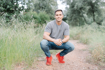 Smiling athletic man crouching on way looking at camera