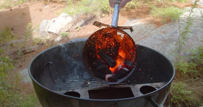 Hand picking up and dumping out red hot charcoal lumps into the smoker port of a kettle grill