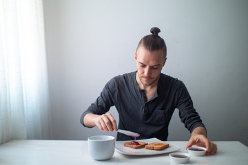 Blond Caucasian Man Preparing Toast with Fruit Jam on a White Table