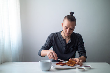 Blond Caucasian Man Preparing Toast with Fruit Jam on a White Table