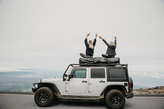 Female friends enjoying view while sitting on top of SUV at Maui, Hawaii, USA