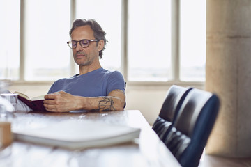 Senior man sitting at the table in a loft flat reading a book