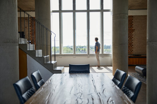 Wooden table in a loft flat with man at the window in background