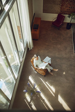Senior man sitting on chair in a loft flat reading newspaper