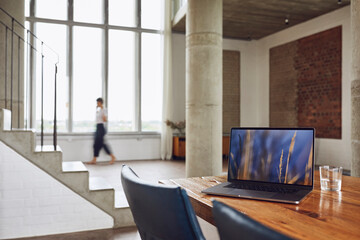 Laptop on wooden table in a loft flat with woman in background