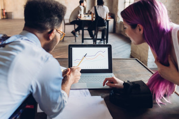 Two creative business people hanalyzing chart on laptop screen in loft office