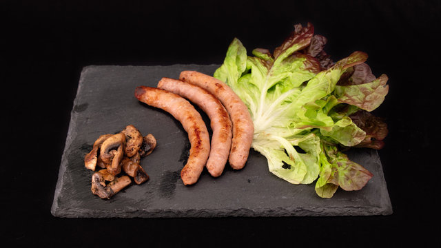 
Sausages, salad and mushrooms on a slate, all on a black background