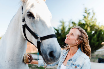 Smiling woman brushing a horse on a farm