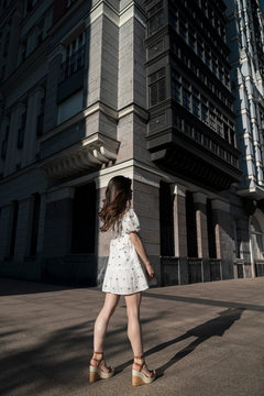 Young woman in white mini dress standing on city street during sunny day