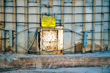 Close-up of a bright yellow caution sign hanging over a hatch at the base of an old concrete silo...