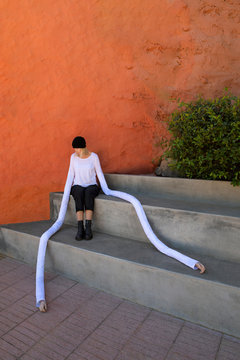 Woman with artificial long hands sitting on concrete steps by plants