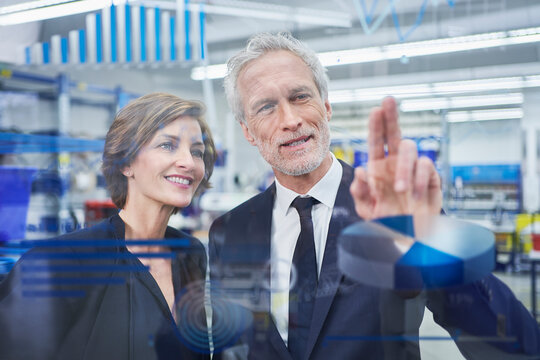 Male and female managers analyzing graphs on glass in factory