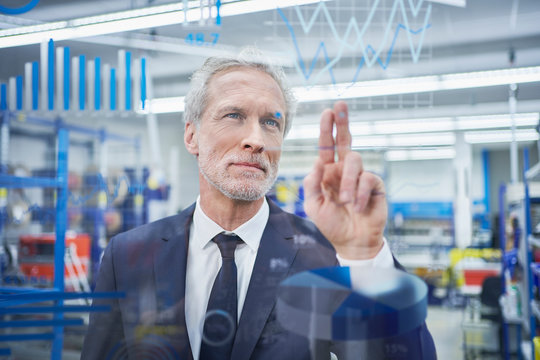 Confident male manager touching line graph on glass in industry