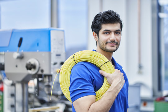 Confident male worker carrying rolled up cables in factory