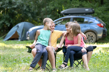 Happy young family enjoying time at capmsite outdoors. Parents and their kids sitting together and talking happily.