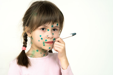 Child girl covered with green rashes on face ill with chickenpox, measles or rubella virus holding...