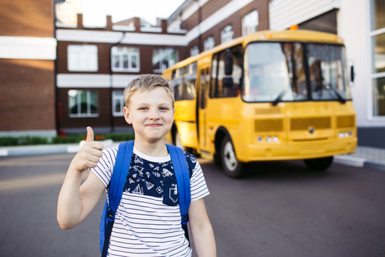Smiling School Boy from elementary school shows a thumbs up in front of school bus. Back to school. Education. Day of knowledge.