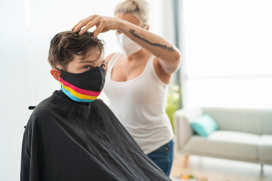 Female hairdresser wearing mask cutting boy's hair at home during curfew