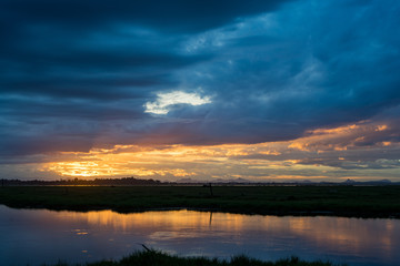 Storm clouds over the water with the sunset over the lake. Orange sunlight, dramatic sky with clouds. Beautiful reflections in water