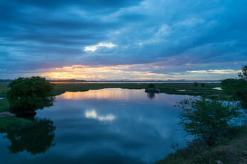 Storm clouds over the water with the sunset over the lake. Orange sunlight, dramatic sky with clouds. Beautiful reflections in water