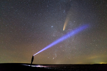 Silhouette of a man with flashlight on his head pointing bright beam of light on starry sky with...