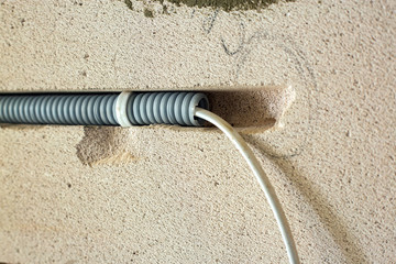 Electrical cables laid in protective corrugation installed on the ceiling and wall in a room under construction works.