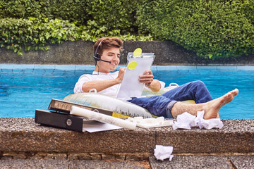 Young man sitting on airbed in swimmingpool and working