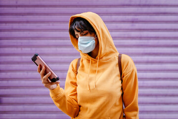 Portrait of young woman with yellow hoodie and protective mask in front of purple background