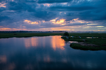 Storm clouds over the water with the sunset over the lake. Orange sunlight, dramatic sky with clouds. Beautiful reflections in water