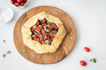 Zucchini and grape tomato galette topped with fresh oregano on a circular wooden cutting board.