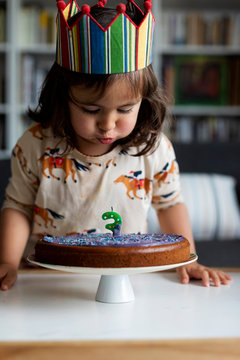 Naklejki Portrait of little girl blowing out candle on her birthday cake at home