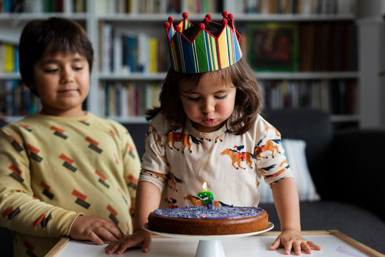 Portrait of little girl blowing out candle on her birthday cake at home