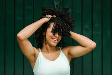 Happy young woman with hand in black curls while standing against green metal door
