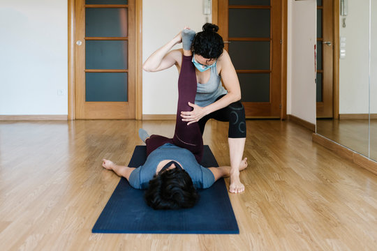 Physiotherapist wearing mask stretching patient's leg lying on exercise mat