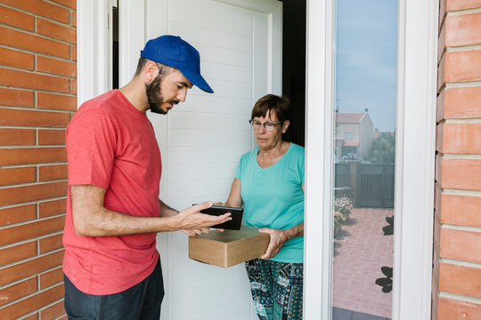 Postal worker showing digital tablet to senior woman for signature at doorway