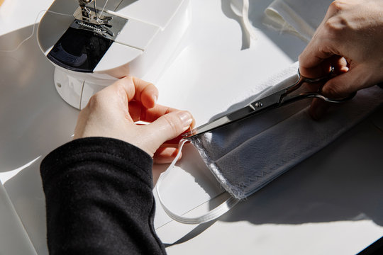 High angle of crop female cutting thread in a fabric protective face mask at home