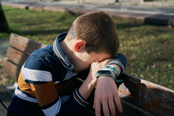 child on a bench covers his face with his arm and is crying