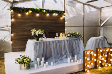 Festive table decorated with composition of flowers and greenery, candles in the wedding banquet hall. Table newlyweds covered with a tablecloth and served with dishes and cutlery.