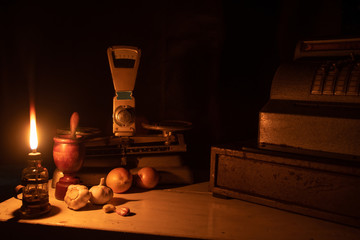 cash register, scale, spices and old money lit by the flame of an old lamp on wooden table, "Low Key" image selective focus.