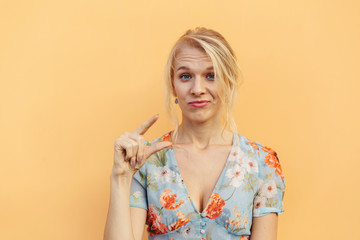 Small amount. Head shot portrait girl showing little size gesture with fingers isolated on orange...