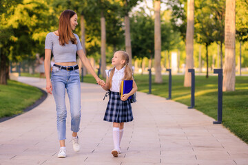 happy mother takes little daughter schoolgirl to school