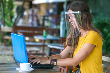 woman sitting in empty cafe wearing protective visor