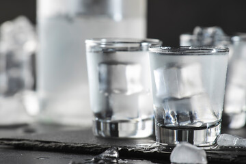 Vodka in shot glasses on black stone background, iced strong drink in misted glass