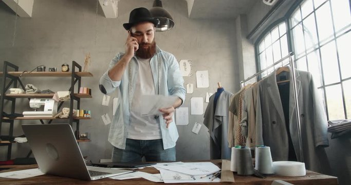 Cool hipster designer working in his office, talking or recording voice message on phone, making an order, customer service - fashion, small business concept 4k footage