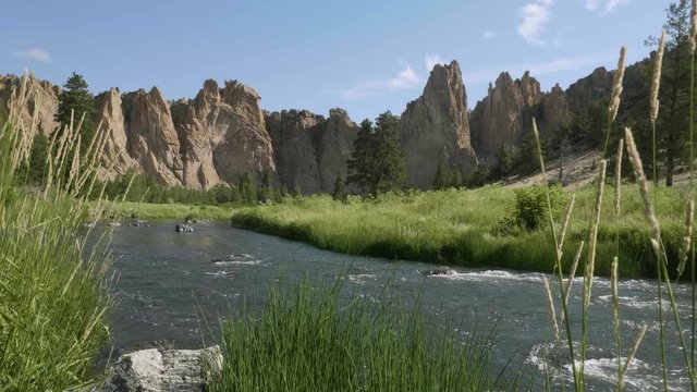 Tall desert orange dry rock cliff mountain landscape with winding water river tall vibrant green grass and cattails sunny day smith rock state park central oregon usa tracking forward slow motion