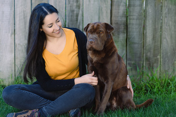 Young hispanic woman sitting on the grass with his pet, a labrador Shar Pei mix.