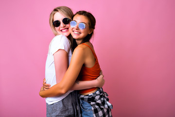 Positive studio portrait of two happy sister best friend woman hugs smiling and screaming together, simple casual outfits and sunglasses, friendship goals.