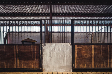Old box for animals in an empty stable with bars and wooden doors for horses.
